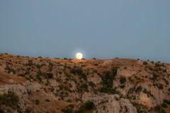 The nascent moon rising over a mountain